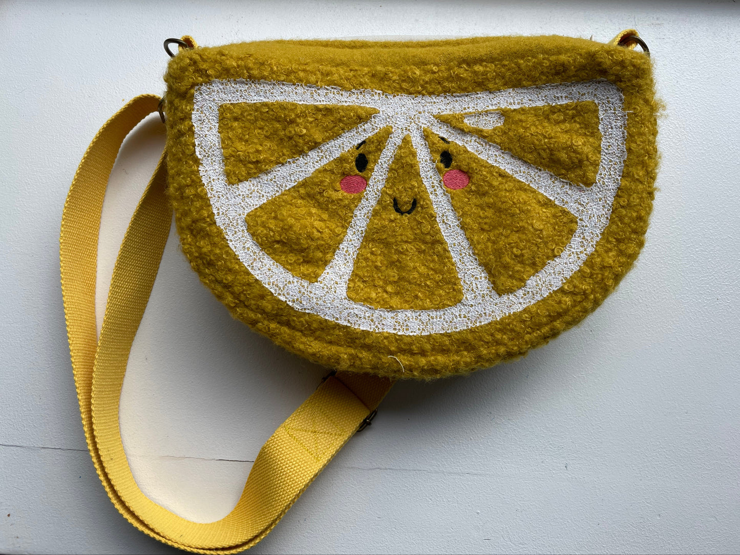 Embroidered lemon slice purse with a face on a white background