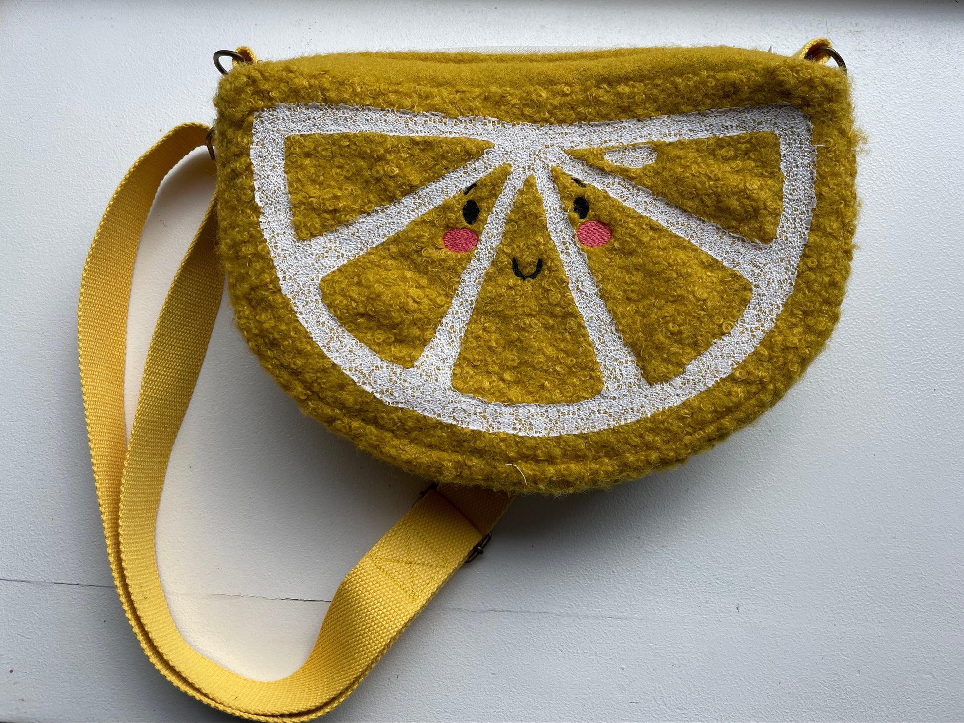 Embroidered lemon slice purse with a face on a white background